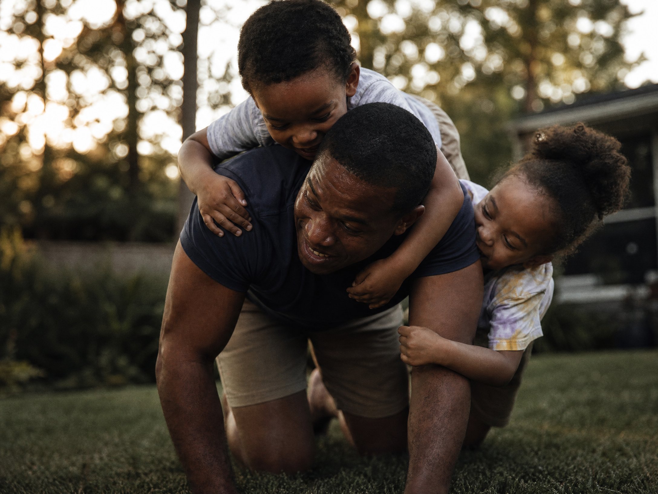 Father playfully carrying and moving with his young children in the yard